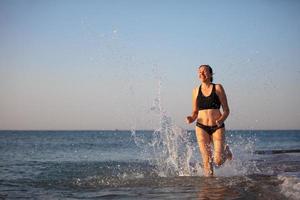 een middelbare leeftijd vrouw loopt langs de oever. aan het doen sport- Bij zee. foto