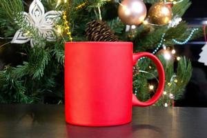 blanco rood mok met Kerstmis boom Aan achtergrond, mat thee of koffie kop met Kerstmis en nieuw jaar decoratie, verticaal bespotten omhoog met keramisch mok voor heet drankjes, leeg geschenk afdrukken sjabloon foto