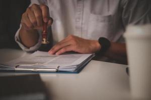 zakenman hand- stempelen goedgekeurd Aan certificaat document contract in kantoor. advocaat stempelen toestaan Aan papierwerk Bij houten bureau. foto