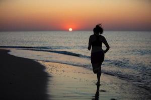 silhouet van een vrouw atleet Aan een achtergrond van zonsopkomst Bij zee foto