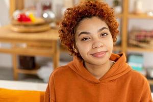 mooi Afrikaanse Amerikaans meisje met afro kapsel glimlachen zittend Aan sofa Bij huis binnen. jong Afrikaanse vrouw met gekruld haar- lachend. vrijheid geluk zorgeloos gelukkig mensen concept. foto