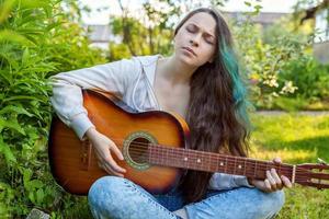 jong vrouw zittend in gras en spelen gitaar foto