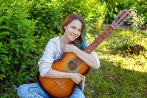 jong vrouw zittend in gras en spelen gitaar foto