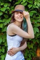 mooi jong hipster brunette meisje in hoed met lang groen haar- glimlachen Aan park achtergrond foto