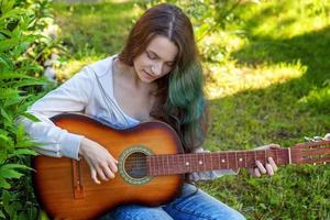 jong vrouw zittend in gras en spelen gitaar foto