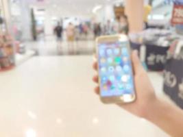 hand- Holding mobiel slim telefoon in boodschappen doen winkelcentrum, vervagen achtergrond foto