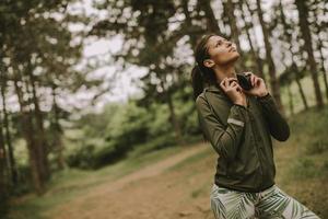 jonge mooie vrouwelijke atleet luisteren naar muziek en een pauze nemen na het joggen in een bos foto