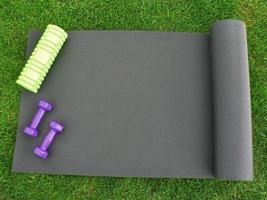 houden fit en oefenen buitenshuis of Bij huis. Purper halters, groen schuim rollen Aan een yoga mat Aan groen gras gazon in een achtertuin of park. gezond levensstijl. kopiëren ruimte. foto