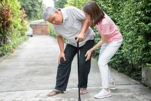Aziatisch senior Mens wandelen in de achtertuin en pijnlijk ontsteking en stijfheid van de gewrichten artritis en de dochter kwam naar helpen steun. concept van oud ouderen verzekering en Gezondheid zorg foto