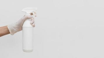 hand met handschoen met reinigingsoplossing in fles met kopie ruimte op witte achtergrond foto