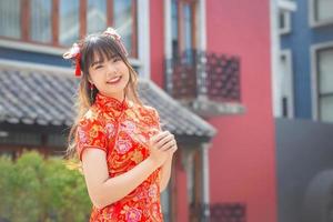 schattig Aziatisch jong vrouw in rood cheongsam jurk in Chinese nieuw jaar thema staat glimlachen gelukkig op zoek Bij de camera mongo oud stad centrum in Chinese nieuw jaar thema. foto