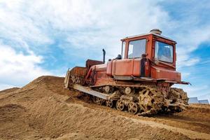 een oud oranje bulldozer presteert werk naar niveau de zanderig bodem foto