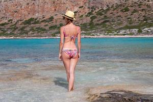 achterzijde visie van een vrouw in een het baden pak wie is staand Aan de strand tegen de backdrop van bergen en de oceaan foto