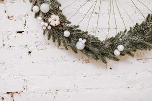 kerstmis, nieuw jaar samenstelling. feestelijk krans met wit ballen gemaakt van Kerstmis boom, Spar takken Aan wit steen muur. Scandinavisch knus huis decor. gelukkig vakantie, sjabloon. groet kaart. 2023 foto