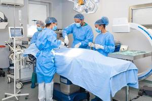 groep van medisch team dringend aan het doen chirurgisch operatie en helpen geduldig in theater Bij ziekenhuis. medisch team het uitvoeren van chirurgisch operatie in een helder modern in werking kamer foto