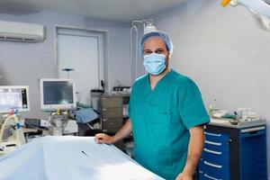 portret van mannetje chirurg in operatie theater op zoek Bij camera. dokter in scrubs en medisch masker in modern ziekenhuis in werking kamer. foto