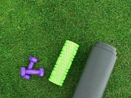 houden fit en oefenen buitenshuis of Bij huis. Purper halters, groen schuim rollen Aan een yoga mat Aan groen gras gazon in een achtertuin of park. gezond levensstijl. kopiëren ruimte. foto