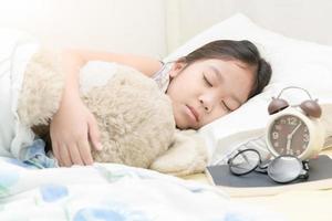 schattig weinig Aziatisch meisje slaap en knuffel teddy beer Aan bed foto