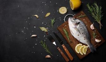 rauw geheel dorado vis Aan houten keuken bord en specerijen voor Koken, top visie Aan zwart tafel foto