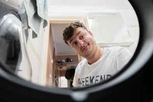 Mens visie van het wassen machine binnen. mannetje doet wasserij dagelijks routine. verrast gelaats uitdrukking. foto