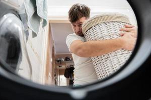 Mens met mand, visie van het wassen machine binnen. mannetje doet wasserij dagelijks routine. foto