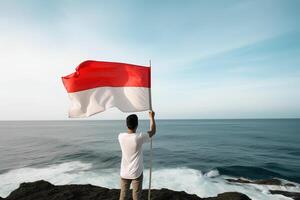 een Mens Holding een rood en wit Indonesië vlag op zoek Bij de oceaan. ai gegenereerd foto