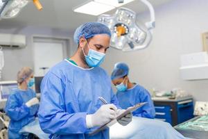 chirurg schrijven Aan klembord in operatie kamer, anesthesist schrijven de updates foto