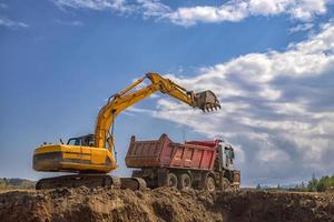 geel graafmachine en leeg dump vrachtauto werken Bij de bouw plaats foto