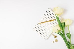 een boeket van voorjaar geel tulpen, een notitieboekje Aan een wit achtergrond en een gouden pen. de concept van lente, vrouwen en moeder dag, verjaardag of bloggen. kopiëren ruimte foto