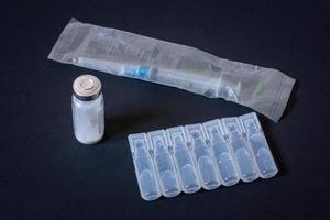 verpakking van plastic ampullen, een beschikbaar injectiespuit in een pakket en een flacon met wit poeder. donker achtergrond. horizontaal. foto