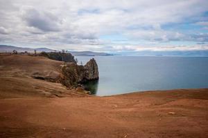 verbazingwekkend kaap Aan de achtergrond van meer Baikal. rotsachtig oever. de lucht is bewolkt. de water is kalm. horizontaal. foto