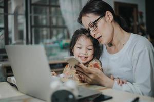 Aziatische vrouw die haar dochter met laptop en smartphone onderwijst, online concept bestudeert. foto
