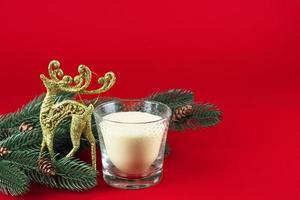Kerstmis kaart. takken van een Kerstmis boom met kegels, een gouden glimmend hert en een wit kaars in een glas glas. foto