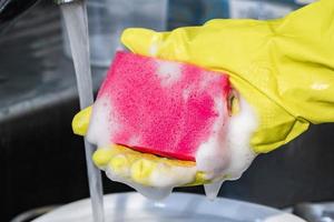 het proces van het afwassen van vuile vaat. een vrouw in een gele rubberen handschoen houdt een roze spons met schuim vast.