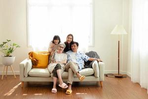 gelukkig familie Aziatisch familie, ouders en kinderen gelukkig zittend Aan de sofa in de huis. de familie ontspant Aan de sofa in de leven kamer. gelukkig familie foto