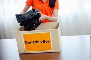 vrouw zetten kleren in een bijdrage doos. helpen de arm liefdadigheid concept en helpen. doorsturen en geven cadeaus naar de arm. foto
