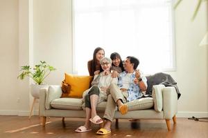 gelukkig familie Aziatisch familie, ouders en kinderen gelukkig zittend Aan de sofa in de huis. de familie ontspant Aan de sofa in de leven kamer. gelukkig familie foto