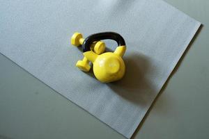 geel kettlebell en geel dumbells houdende Aan de grijs yoga mat foto