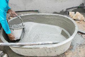 bouwer aannemer Mens baan mengen beton in industrie werk projecteren, gieten nat vloeistof materiaal in de groot menging dienblad in bouw plaats net zo professioneel werk foto
