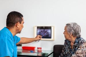 mannetje midden- -bejaard tandarts Bij zijn kantoor gebruik makend van een X straal beeld naar leg uit behandeling naar zijn senior vrouw geduldig foto