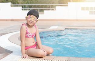 schattig Aziatisch meisje glimlach en zitten Aan zwemmen zwembad. foto