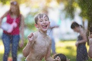 weinig jongen onder de water jets. een kind in de gieten regen. . krijgen onder de waterval. het baden in de stad fontein. foto