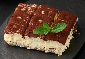 een stuk van tiramisu besprenkeld met cacao, Aan top van een takje van vers munt Aan een zwart achtergrond foto