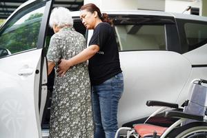 verzorger helpt aziatische bejaarde vrouw met een handicap om in haar auto te stappen, medisch concept. foto