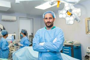 portret van mannetje chirurg staand met armen gekruiste in operatie theater Bij ziekenhuis. team chirurgen zijn het uitvoeren van een operatie, midden- oud dokter is op zoek Bij camera, in een modern in werking kamer foto