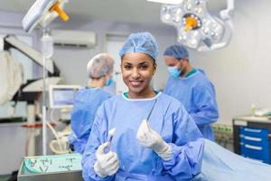 portret van Afrikaanse Amerikaans vrouw chirurg staand in in werking kamer, klaar naar werk Aan een geduldig. vrouw medisch arbeider in chirurgisch uniform in operatie theater. foto