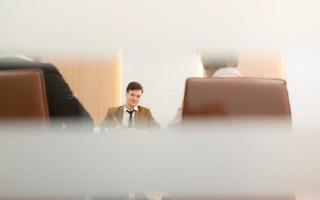Bij de vergadering kamer, een jong zakenman zittend in een geheim vergadering met veel andere zakenlieden de atmosfeer is goed. hebben een gelukkig glimlach foto