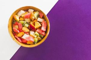 kom met fruitsalade op een witte en paarse achtergrond
