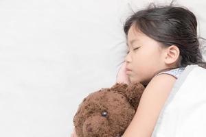 schattig weinig Aziatisch meisje slaap en knuffel teddy beer foto