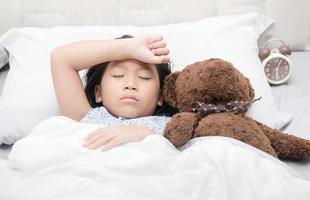 kind meisje slapen en ziek Aan de bed met beer pop foto